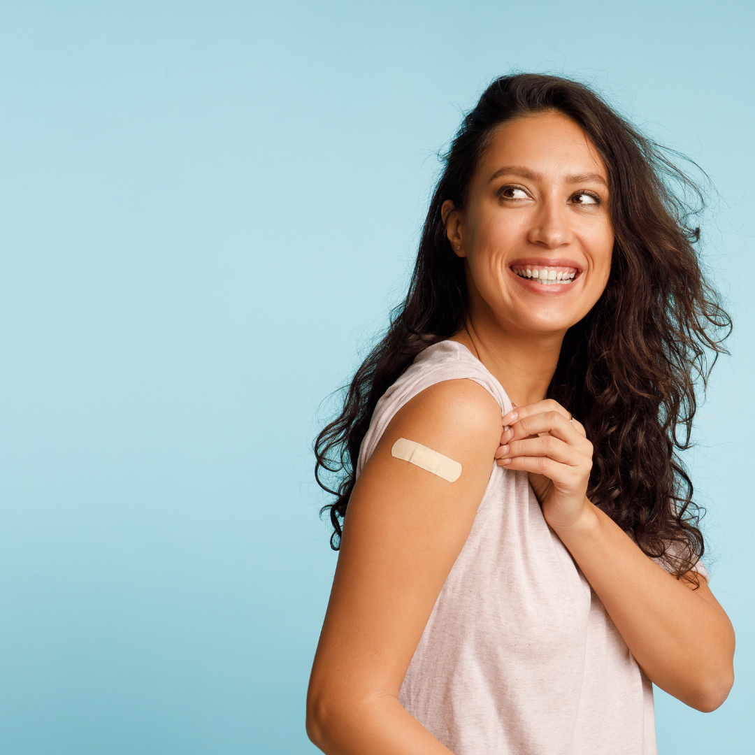 Donna sorridente con un cerotto sul braccio dopo la vaccinazione anti-influenzale, su sfondo azzurro, a rappresentare la prevenzione contro l'influenza stagionale