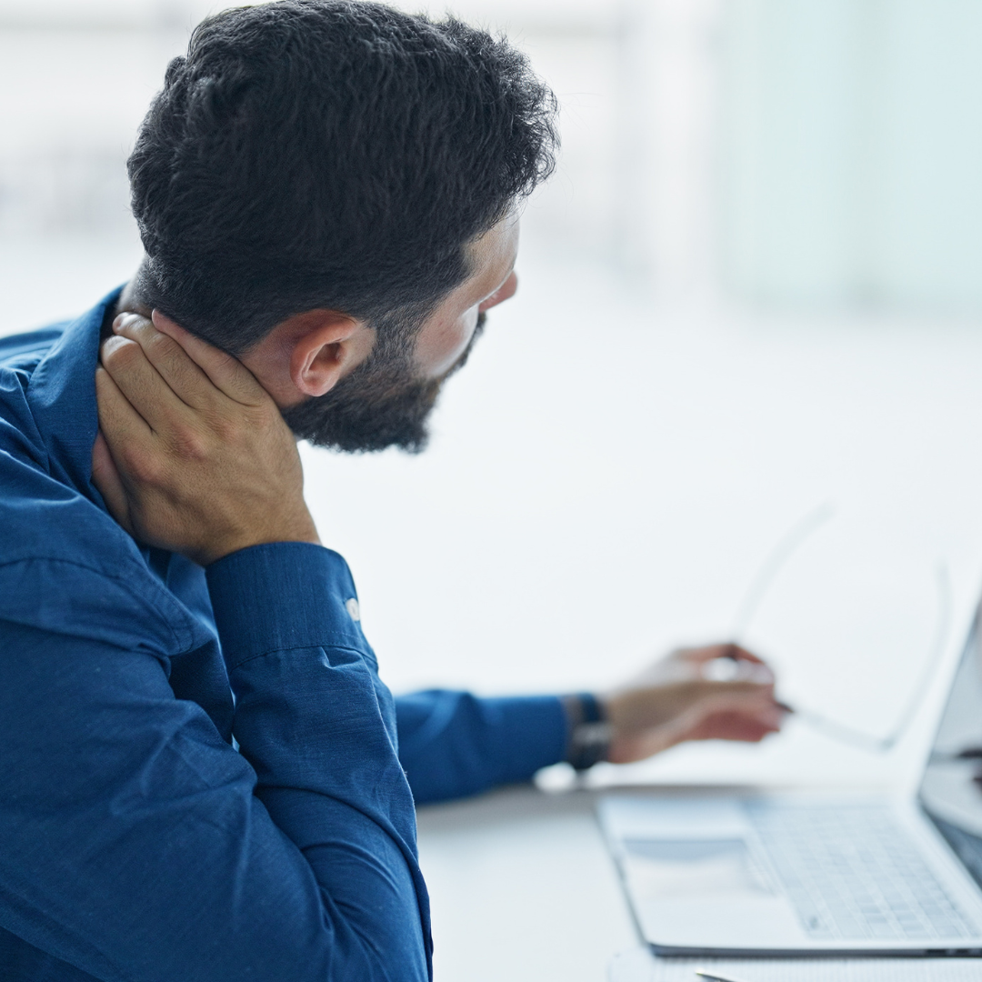 Uomo seduto davanti al computer che si tocca il collo per un fastidio cervicale, a rappresentare tensione e rigidità muscolare legate ai primi freddi