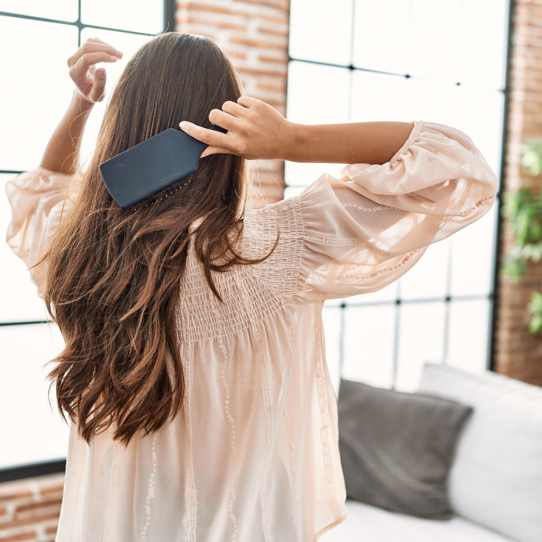 Donna vista di spalle mentre si spazzola i capelli lunghi, a rappresentare la caduta stagionale dei capelli tipica del periodo autunnale